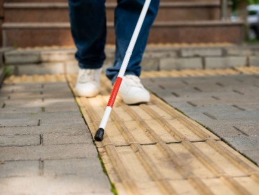 A person using a cane and walking on a tactile ground surface.