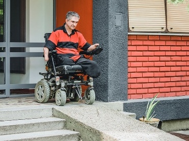 A wheelchair user using an accessibility ramp outside a building.