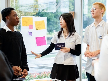 3 people at an event having a conversation. Behind them is a board with notes on it.