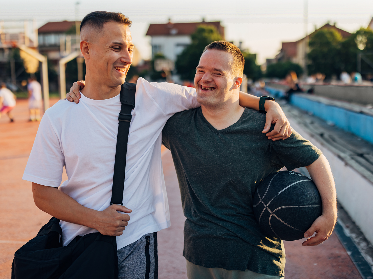2 friends laughing and smiling together. They are outdoors and one is holding a basketball.