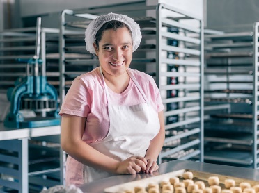 A person smiling and working at a bakery.